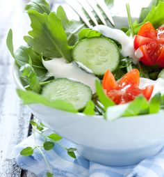 a salad with cucumbers, tomatoes and lettuce in a white bowl