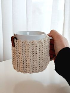 a hand holding a coffee cup in a crocheted mug cozying it up