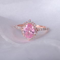 a pink diamond ring sitting on top of a white cloth with diamonds around the band