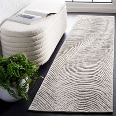 a white rug with wavy lines on the floor next to a plant in front of a window