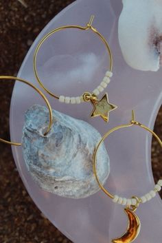 a pair of gold hoop earrings with stars and moon charms sitting on top of a rock