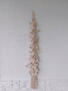 a wall hanging with flowers and tassels attached to it's side on a white brick wall