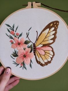 a hand is holding an embroidered butterfly with pink flowers on the back and yellow wings