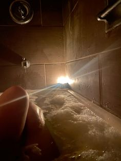 the person is taking a bath in the tub with their feet on the edge and light coming from behind them