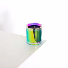 a candle that is sitting on top of a white table next to a vase with a green, purple and yellow liquid in it