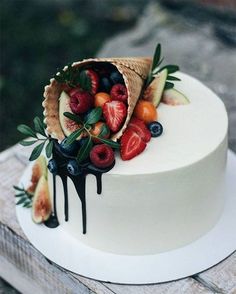 a white cake with fruit on top and chocolate dripping down the side is sitting on a wooden table