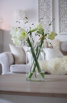 some flowers are in a glass vase on a table near a couch and rugs