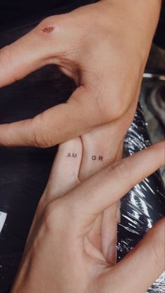 two hands holding each other with small tattoos on their thumbnails and one has the word love written on it