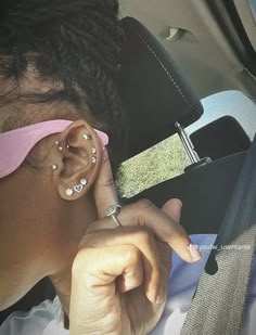 a woman with ear piercings sitting in the back seat of a car looking at her cell phone