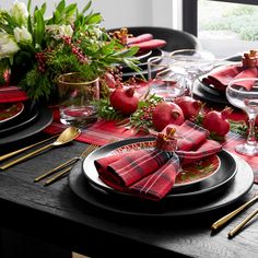 the table is set with red and black plates, napkins, silverware, and flowers