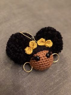 a crocheted doll with black hair and gold hoop earrings sitting on a gray surface