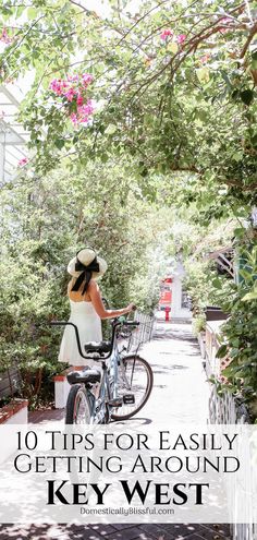 a woman in white dress and hat riding a bike down a sidewalk with trees on both sides