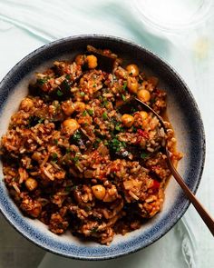 a bowl filled with rice and vegetables on top of a white table next to a spoon