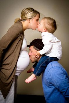 a woman kissing a man's face while holding a baby in front of him