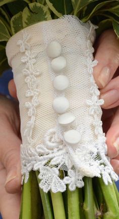 a person holding asparagus wrapped in white lace and buttons with green leaves around them