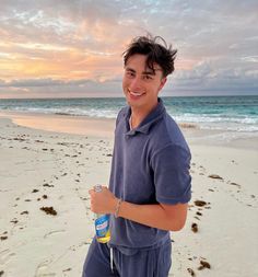 a man standing on top of a beach next to the ocean holding a bottle of water