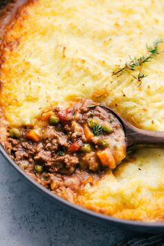 a casserole dish with meat and vegetables in it being stirred with a wooden spoon