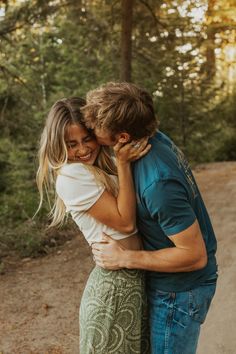 a young man and woman embracing each other in the middle of a dirt road surrounded by trees