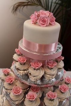 a three tiered wedding cake with cupcakes on the bottom and pink roses on top