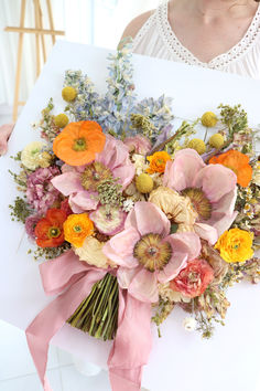 a woman holding a bouquet of flowers on top of a piece of paper in her hands