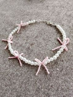 a white bracelet with pink bows and pearls on the bottom is laying on a gray surface