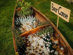 a boat filled with lots of beer bottles on top of a lush green field next to a sign that says deer canoe