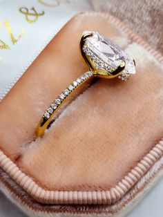 a diamond ring sitting on top of a pink velvet bag with gold trimmings