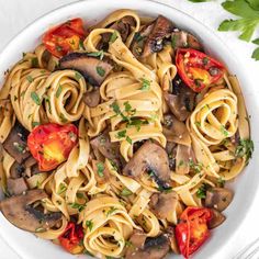 a white bowl filled with pasta, mushrooms and tomato slices on top of a table