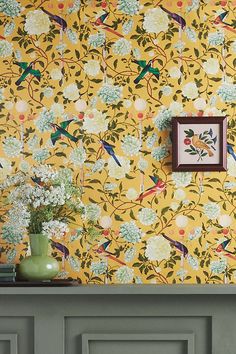 a yellow wallpaper with birds and flowers in front of a green vase on a table