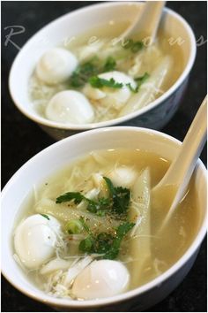 two white bowls filled with soup and three chopsticks in them, on a black surface