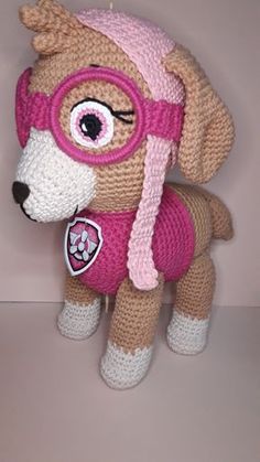 a crocheted stuffed dog with goggles and a pink hat on it's head