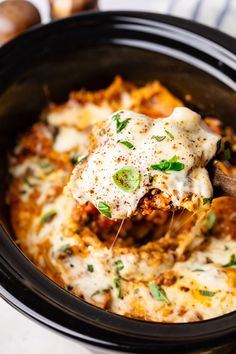 a wooden spoon scooping some food out of a crock pot filled with pasta