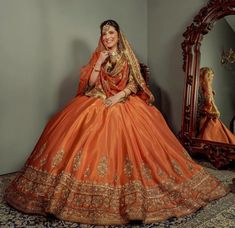 a woman in an orange and gold wedding gown sitting on a rug with a mirror behind her