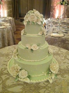 a three tiered green wedding cake sitting on top of a table with white flowers