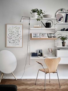 a room with a chair, desk and shelves on the wall above it are plants