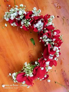 a wreath made out of red roses and baby's breath on a wooden floor