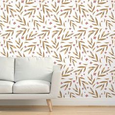 a white couch sitting in front of a wall with brown and red leaves on it