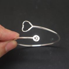 a hand holding a silver bracelet with two hearts and a paw in the middle, on a black surface