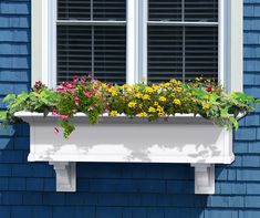 a window box filled with colorful flowers next to a blue building and white trimming