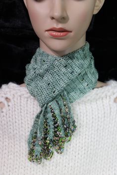 a mannequin head wearing a white sweater and green knitted scarf with sequins