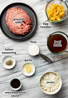 ingredients to make an italian dish on a marble counter top, including ground beef, egg noodles, garlic, and broth