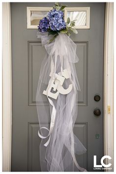 a door hanger decorated with blue flowers and white ribbon hanging from it's front door