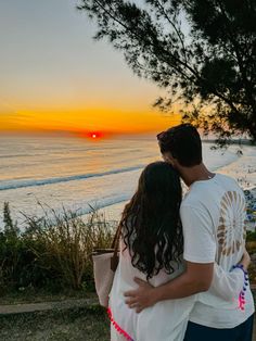 a man and woman standing next to each other near the ocean at sunset or sunrise