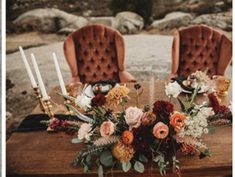 the table is set with two velvet chairs and flowers on it, along with candles