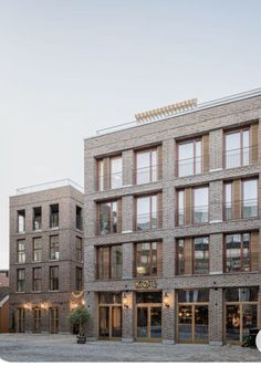 a brick building with many windows on the top floor and two stories above it, in front of a cobblestone street