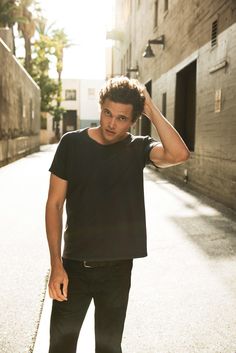 a young man is standing in an alley way with his hand on his head and looking at the camera