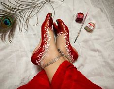 a woman's feet wearing red shoes with white designs on them, next to a peacock feather