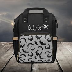 a black and white diaper bag with bats printed on it, sitting on a wooden floor