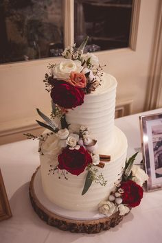 a white wedding cake with red flowers and greenery on the top is sitting on a table