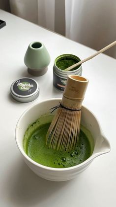 a white bowl filled with green liquid and a wooden whisk